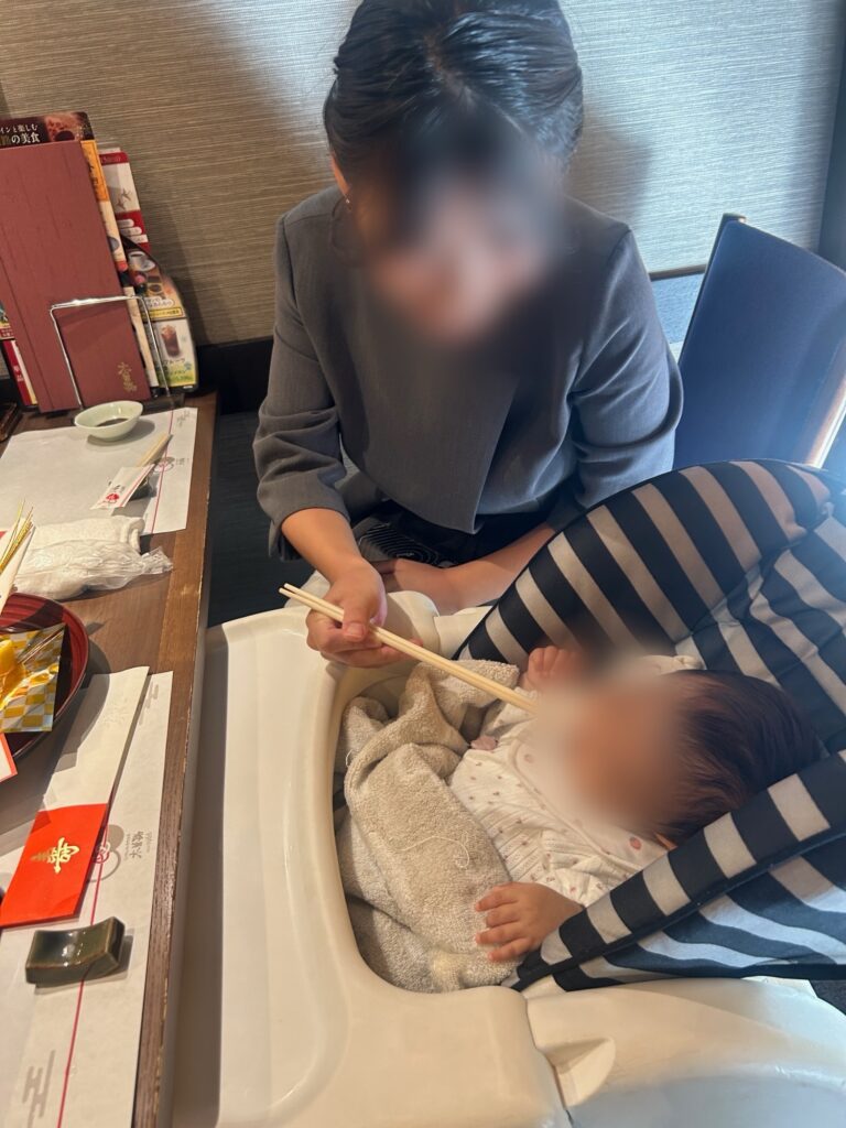 寝ている赤ちゃんにお食い初めの儀式をする母親（顔はぼかし）