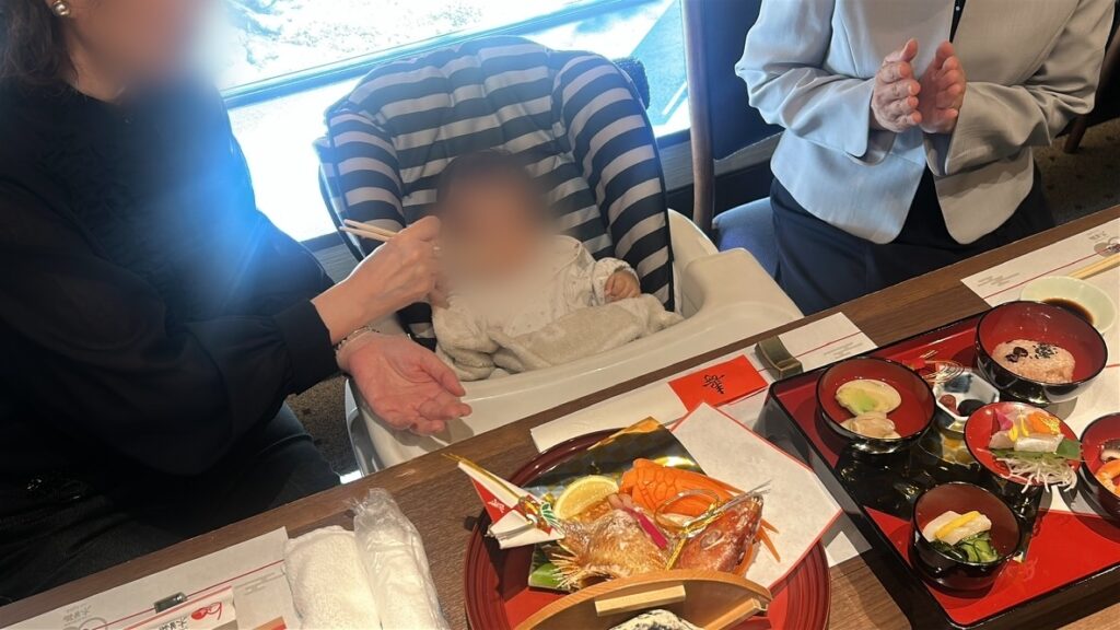祖母が娘にお食い初めの儀式をしているところ（顔はぼかし）